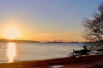 Silhouette man sitting on bench by sea against sky during sunset