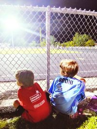 Rear view of a boy looking through chainlink fence