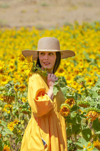 Portrait of young woman standing amidst yellow flowers