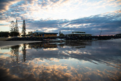 Reflection of buildings in lake against sky during sunset