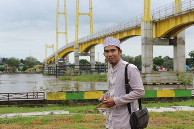 Portrait of young man in traditional clothes standing against bridge 