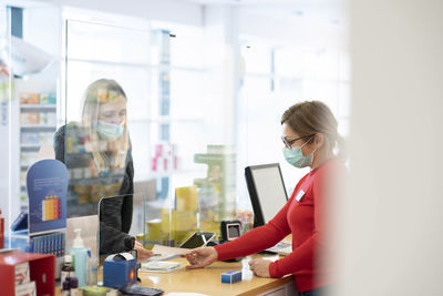 Pharmacist examining prescription of customer at checkout counter