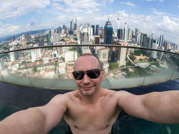 Portrait of shirtless man smiling at balcony against cityscape