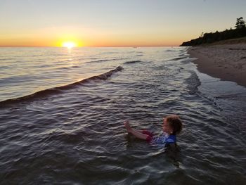 Girl relaxing in sea against sky during sunset