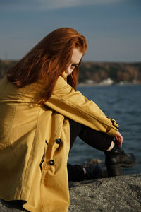 Beautiful woman in coat sitting at beach