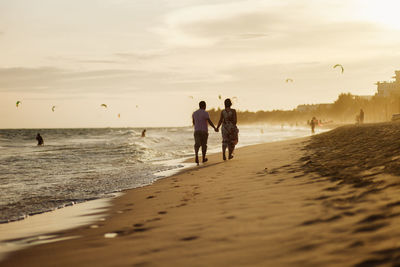 Rear view of couple walking at beach against sky