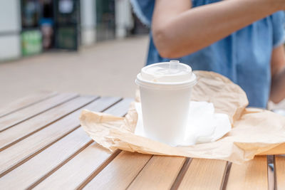 Closeup of woman eating fast food in street cafe, mockup white coffee cup, focus on foreground