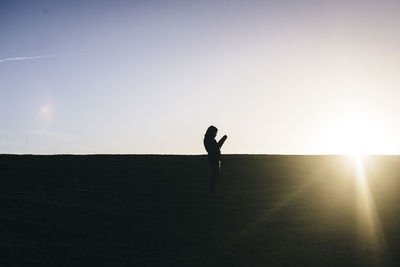 Silhouette man standing on grass against sky during sunset