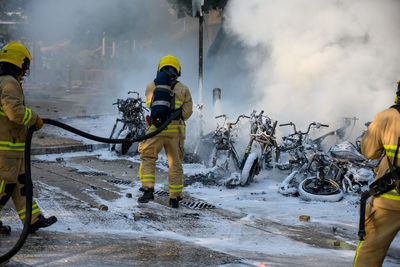 Rear view of firefighters extinguishing burning motorcycles on road in city