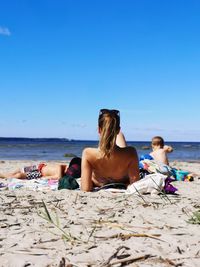 Friends relaxing on beach against clear sky