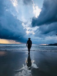 Rear view of silhouette man walking on beach against sky