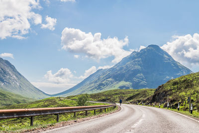 Empty road leading towards mountains against sky