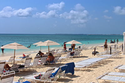 People and deck chairs at beach against sky