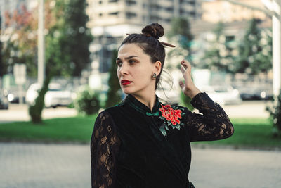 Portrait of young woman standing against trees in a city