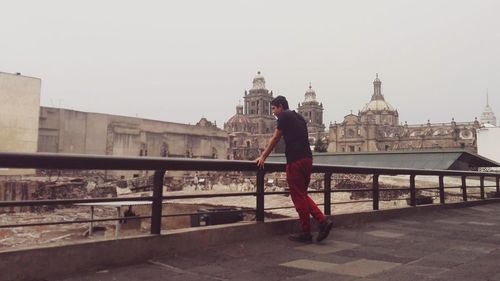 Full length of man standing by railing against buildings in city