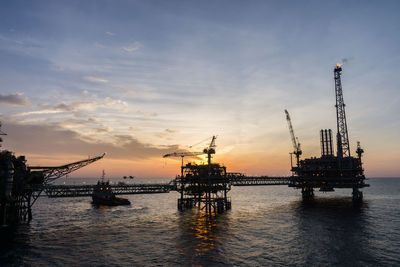 Cranes at commercial dock against sky during sunset