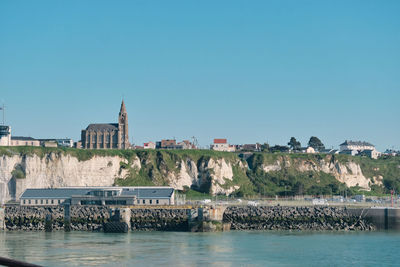 Buildings by sea against clear blue sky