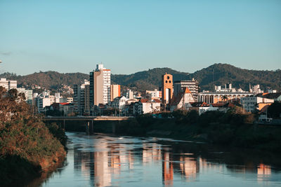 Buildings by river against clear sky