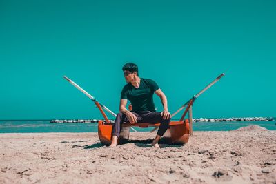 Man sitting on shore at beach against clear sky