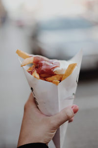 Cropped image of woman hand holding french fries with ketchup in paper bag