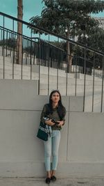 Portrait of young woman standing against railing