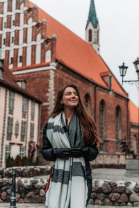 Young woman looking away while standing against building in city