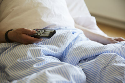 Midsection of senior man using remote control on hospital bed
