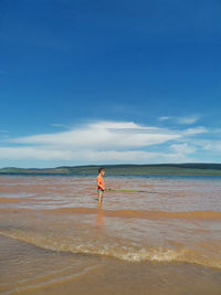 A boy with a fishing rod stands in the river