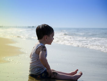 Full length side view of boy sitting on shore at beach