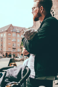 Side view of man carrying son while standing by baby carriage on street