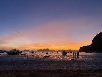 Silhouette boats on beach against sky during sunset