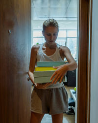 Portrait of a young woman standing against door with the pizza boxes