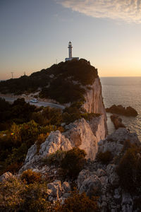 Lighthouse by sea against sky during sunset