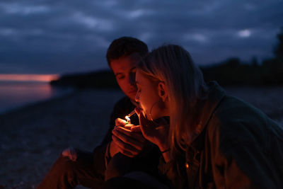 Young couple kissing against sky during sunset