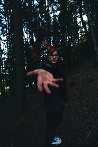 Young man standing by tree trunk in forest