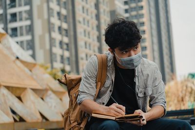 Young man wearing mask writing on diary