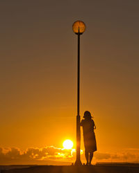 Silhouette man photographing street light against orange sky