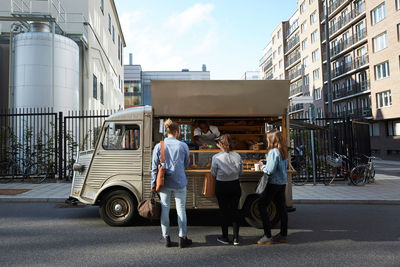 Customers buying bread from salesman at food truck parked on city street