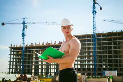 Shirtless man standing against construction buildings