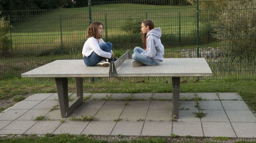 Girls sitting on table tennis table at yard