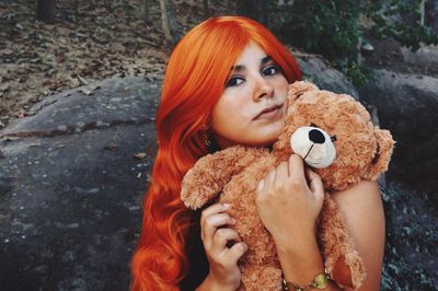 Portrait of young woman with teddy bear against rock