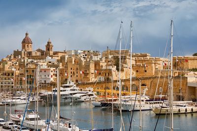 Sailboats moored on harbor by buildings against sky