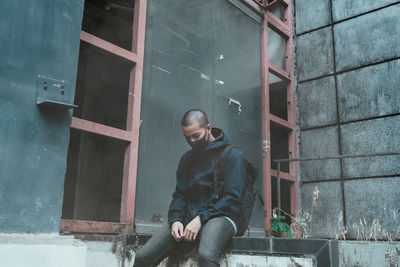 Young man looking away while sitting on window