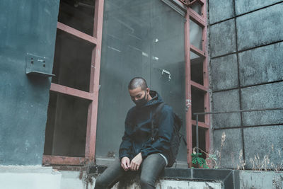 Young man looking away while sitting on window