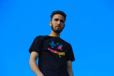 Portrait of young man looking away against blue sky
