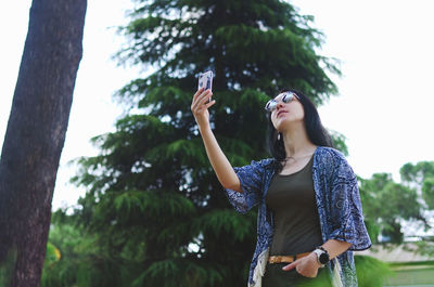 Young woman with arms raised standing against trees