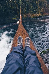 Low section of man sitting on log over river in forest