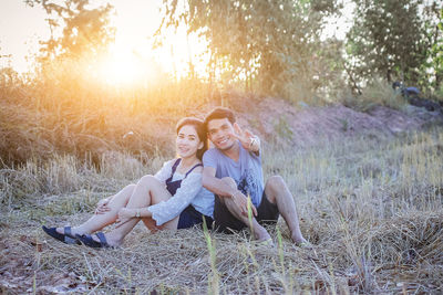 Portrait of happy couple sitting on grassy field during sunset