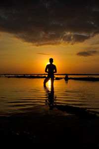 Silhouette man standing at beach against sky during sunset