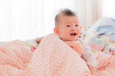 Cute baby boy looking away while sitting on bed in blanket